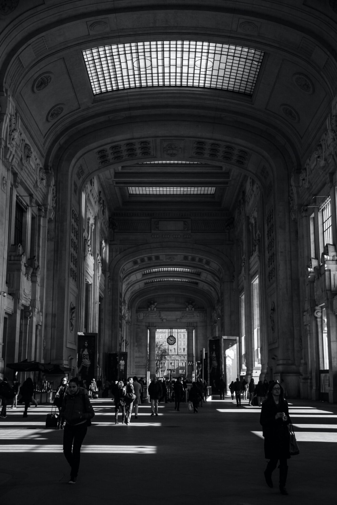 Inside of the high roofed Milan Central Station with detailed walls and roof and people walking in Lombardy Italy in Black and White