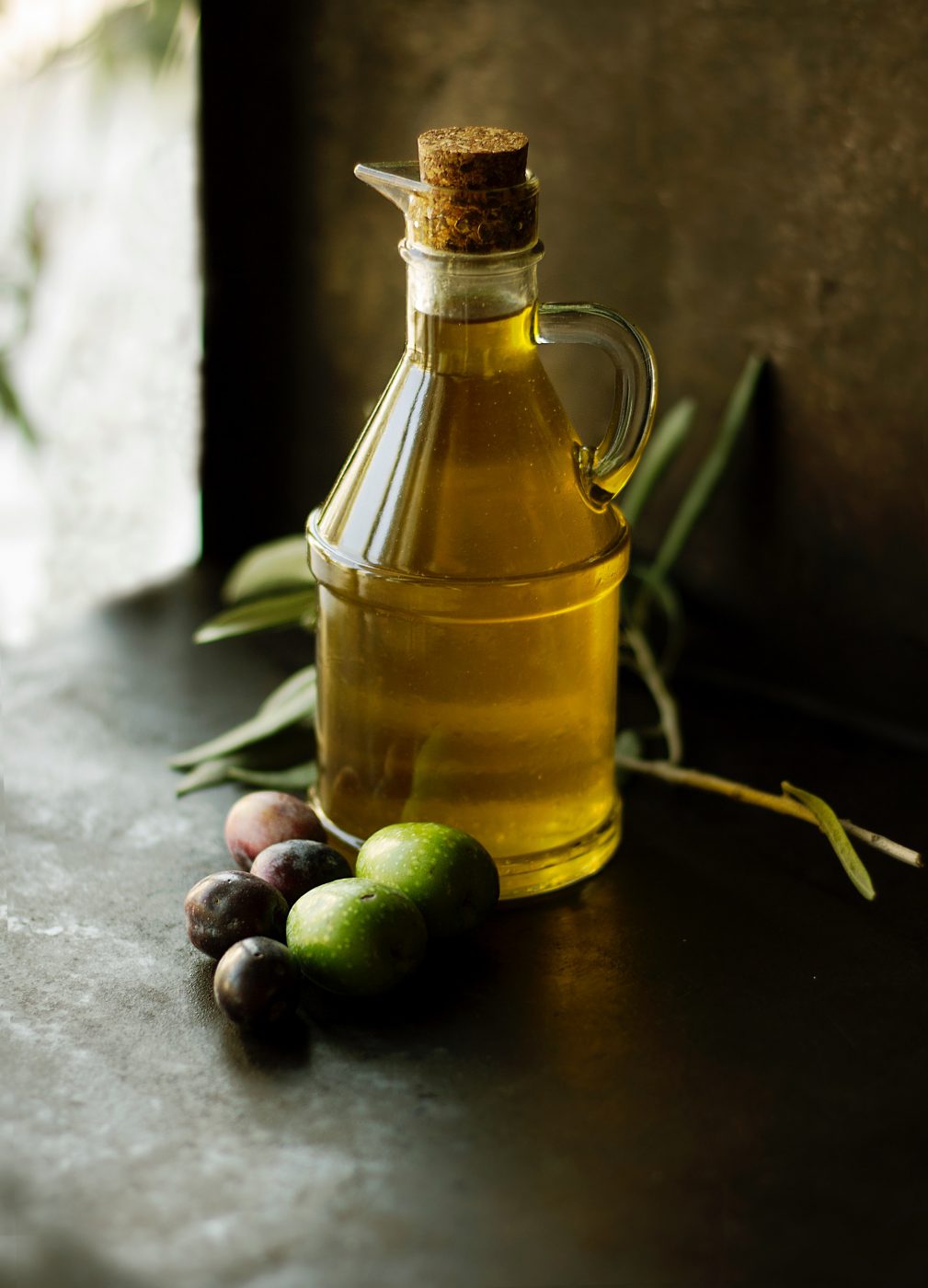 Italian artisan Extra Virgin Olive Oil in glass bottle next to fresh olives in Italy