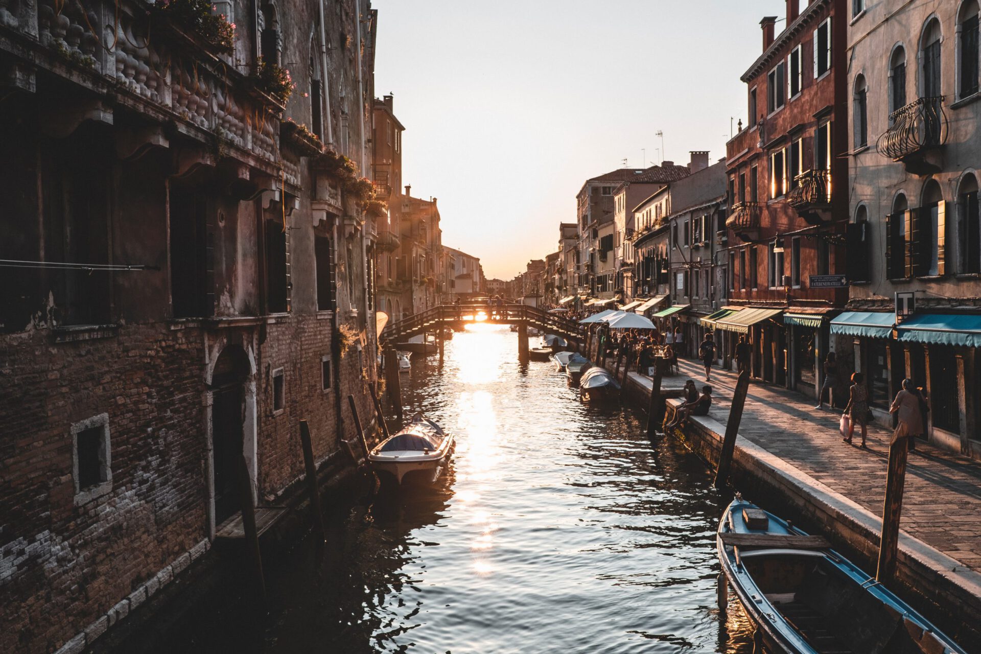 Front view of the Grand Canal filled up with boats and gondolas surrounded by antique and colorful buildings while people walk by Venice Veneto in Italy