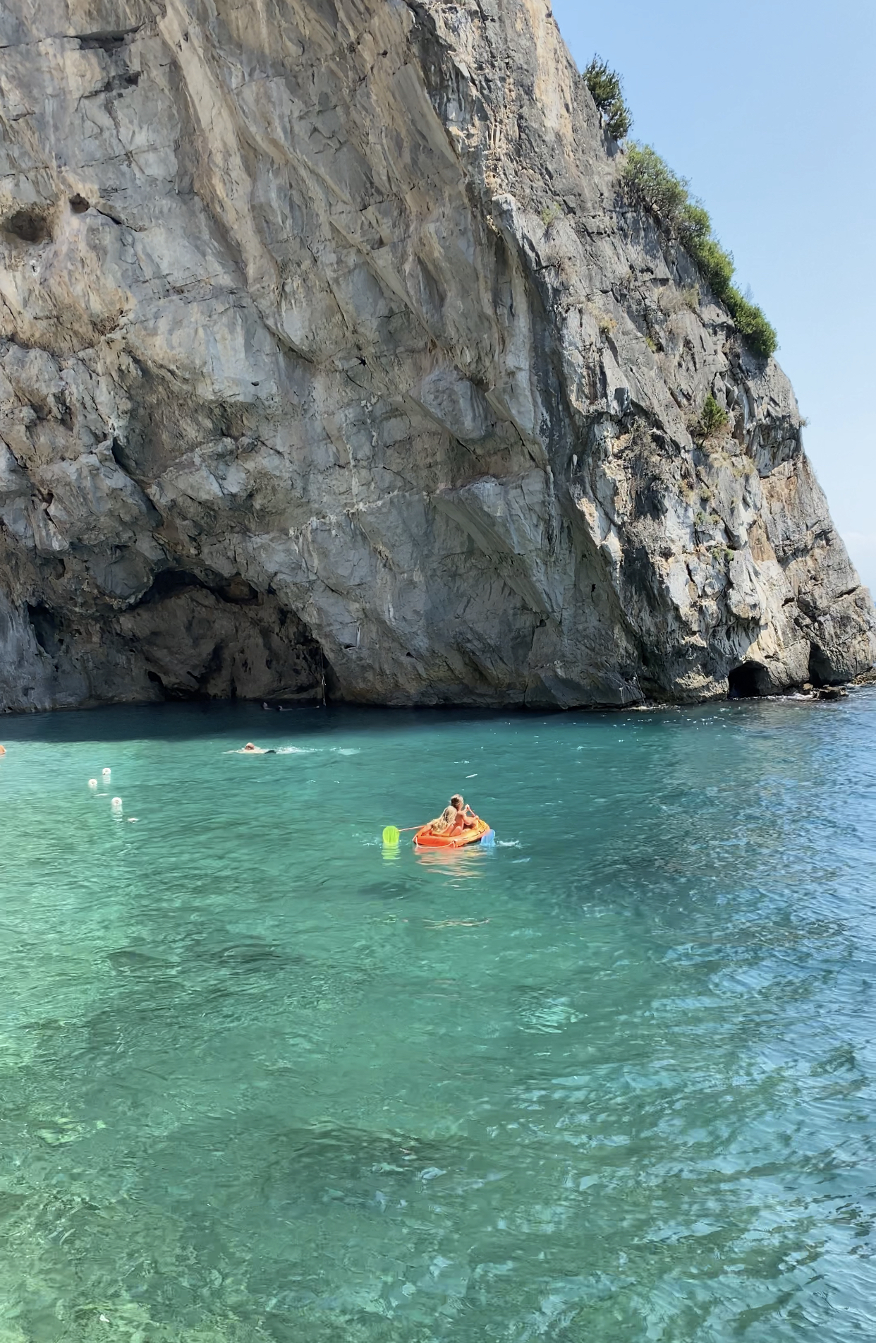 Kids sailing in little colorful boat surrounded by bright clear water behind a high rocky mountain in Conca dei Marini Campania in Italy