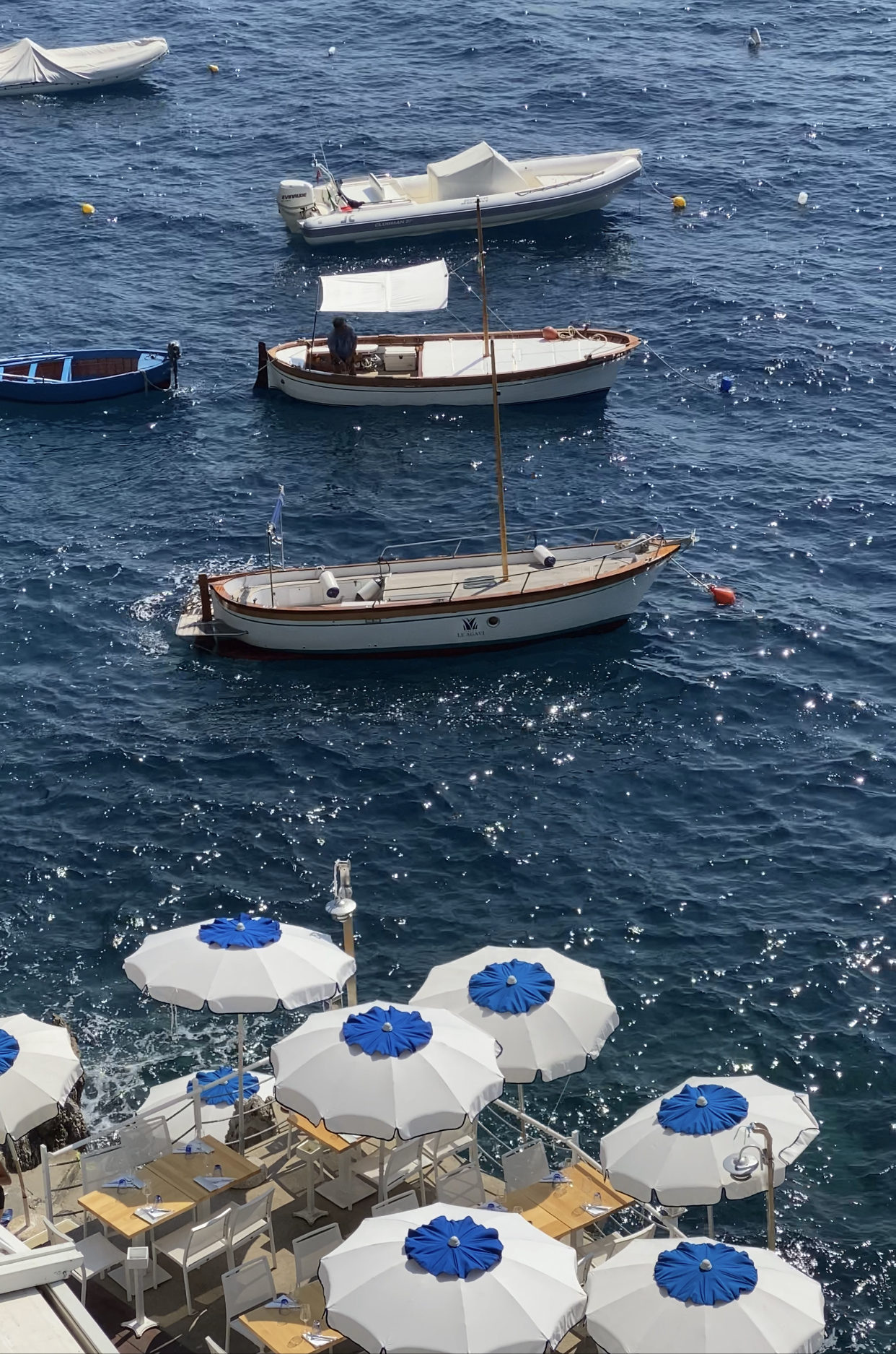 Boats sailing and terrace with umbrellas and chairs over a terrace surrounded by a dark blue ocean in Conca dei Marini Campania in Italy