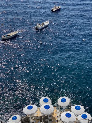 Boats sailing and terrace with umbrellas and chairs over a terrace surrounded by a dark blue ocean in Conca dei Marini Campania in Italy