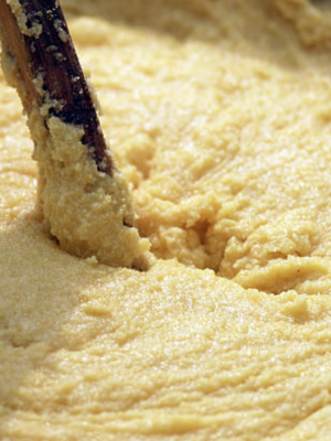 Yellow thick polenta being mixed with a big wooden spoon over huge pot in Italy