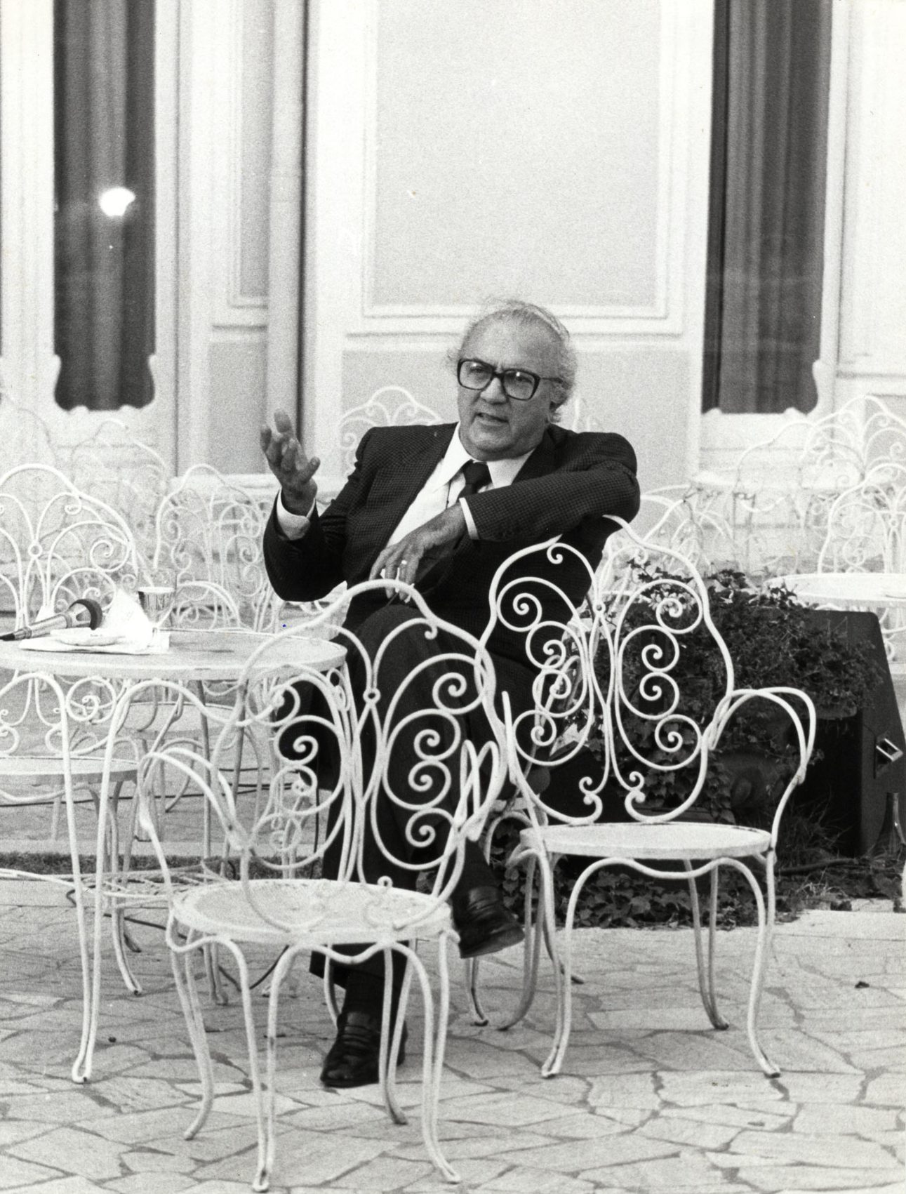 Federico Felini formal dressed with glasses on metallic chairs resting at the Grand Hotel in Rimini Emilia Romagna in black and white in Italy