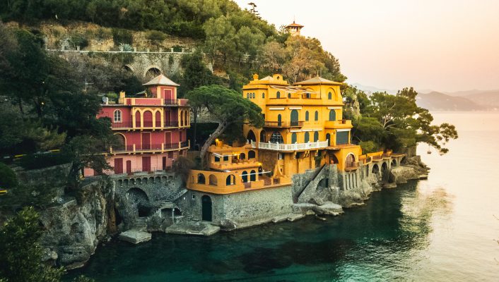 Colorful houses in the middle of a hill over a rocky beach and crystal blue sea surrounded by mountains and plants in Baia Cannone, Liguria in Italy