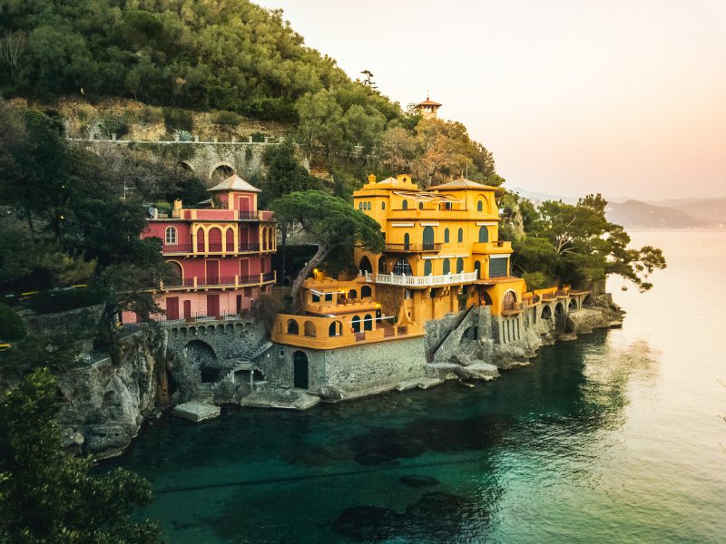 Colorful houses in the middle of a hill over a rocky beach and crystal blue sea surrounded by mountains and plants in Baia Cannone, Liguria in Italy
