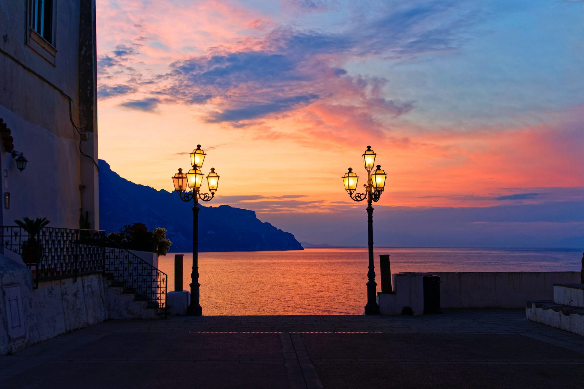 Colorful sunset with red and yellow colored viewed from a deck in the sea and two high urban lamps at Atrani in Campania, Italy