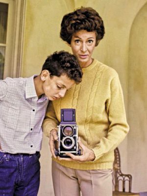 Marella Agnelli with her son filmmaking with an old videocamera with a antique cream colored house behind in Italy