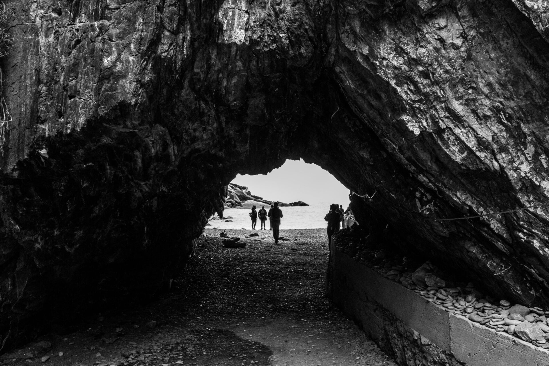 Arch inside a big sharp rock in the beach with people sunbathing in Liguria Italy in Black and white
