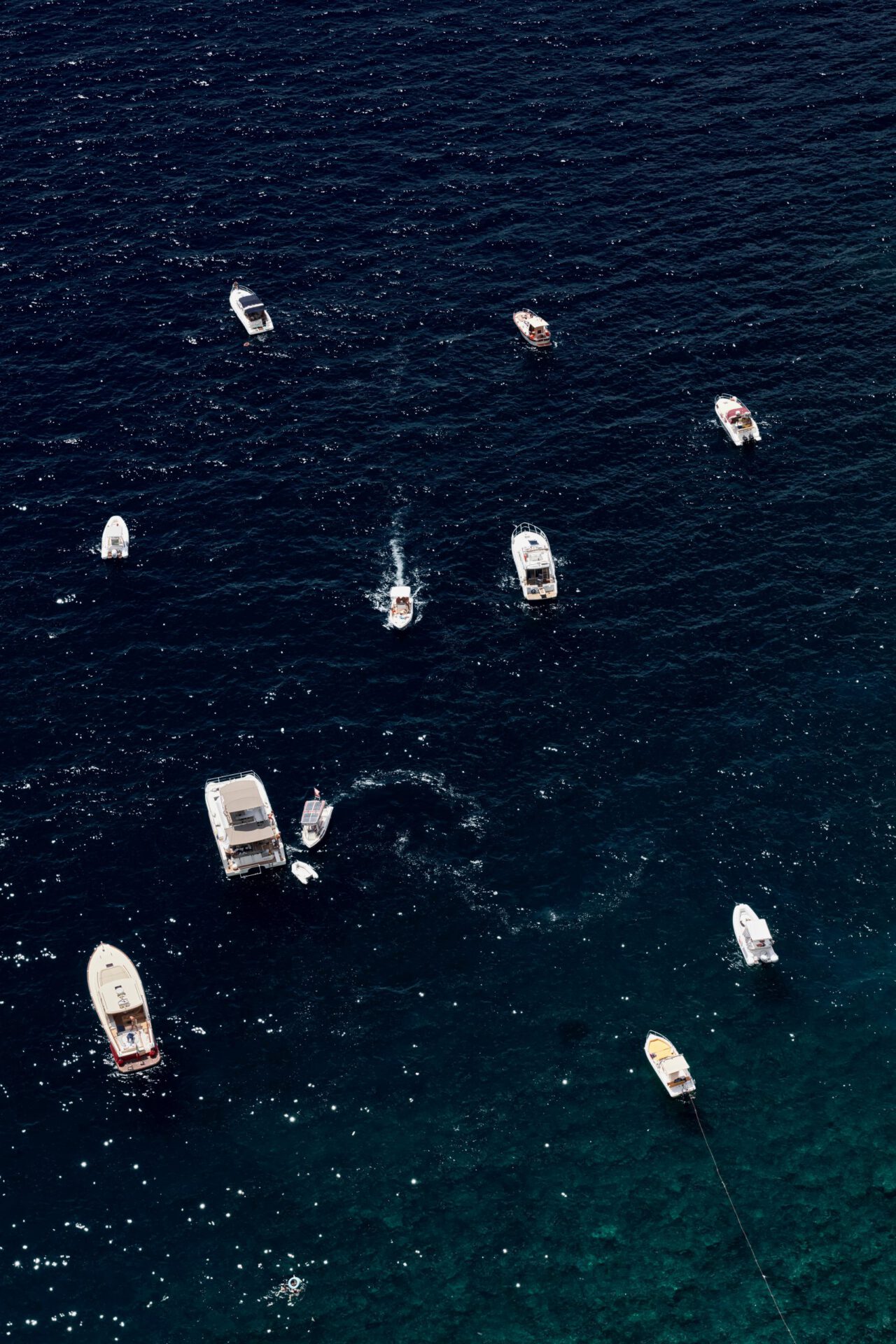 White boats sailing in dark blue ocean with waves and white foam at Vietri Sul Mare in Campania, Italy