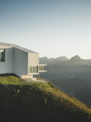 White modern building with big glass windows over the top of a hill surrounded by green grass mountains and blue sky at the Lumen museum in Trentino-Alto Adige in Italy