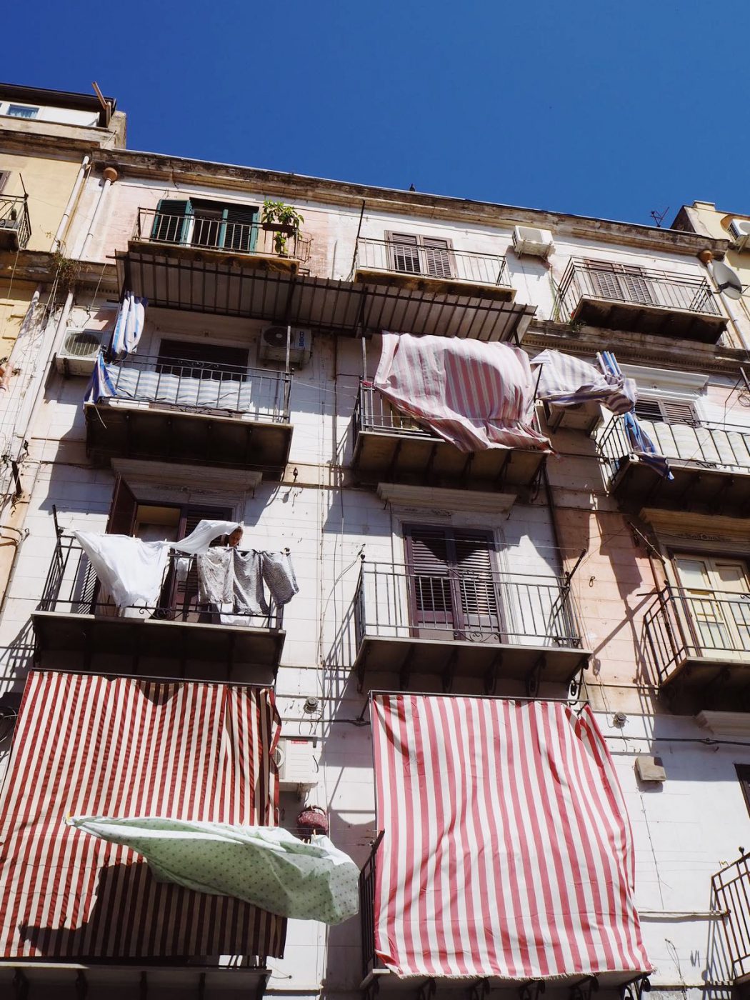 a photo of balconies in Palermo with sheets and clothes hanging on clotheslines and blowing in the wind