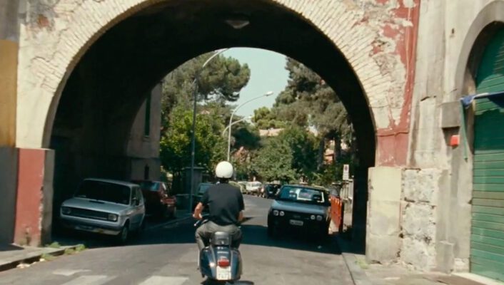 screenshot from Caro Diario of the back of Nanni Moretti riding a vespa under an arch