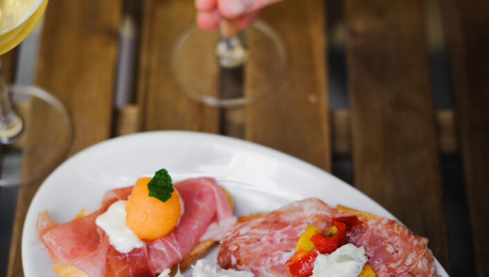 A photo by Valeria Necchio of a small glass of wine and four pieces of bruschetta with different toppings
