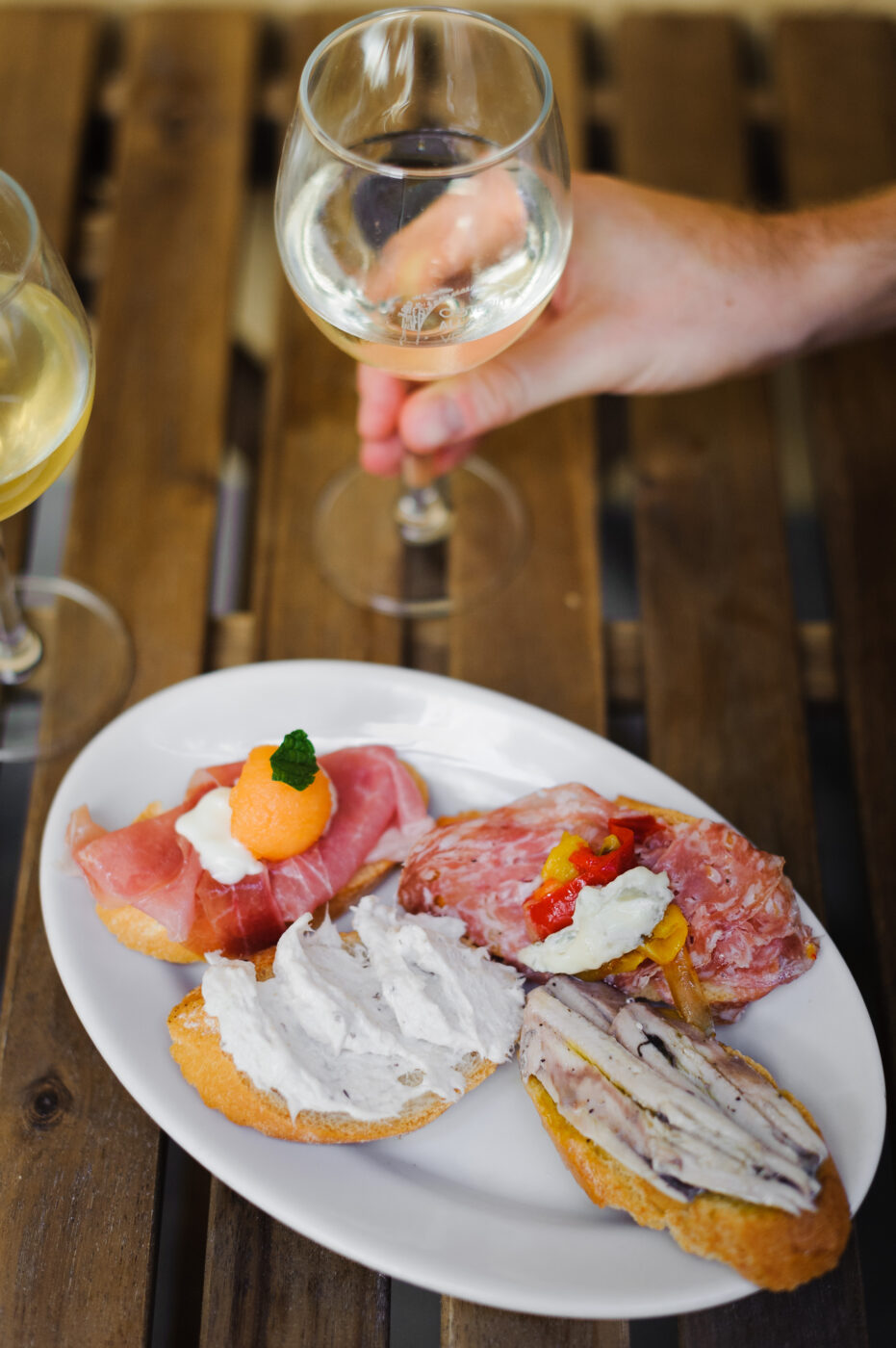 A photo by Valeria Necchio of a small glass of wine and four pieces of bruschetta with different toppings