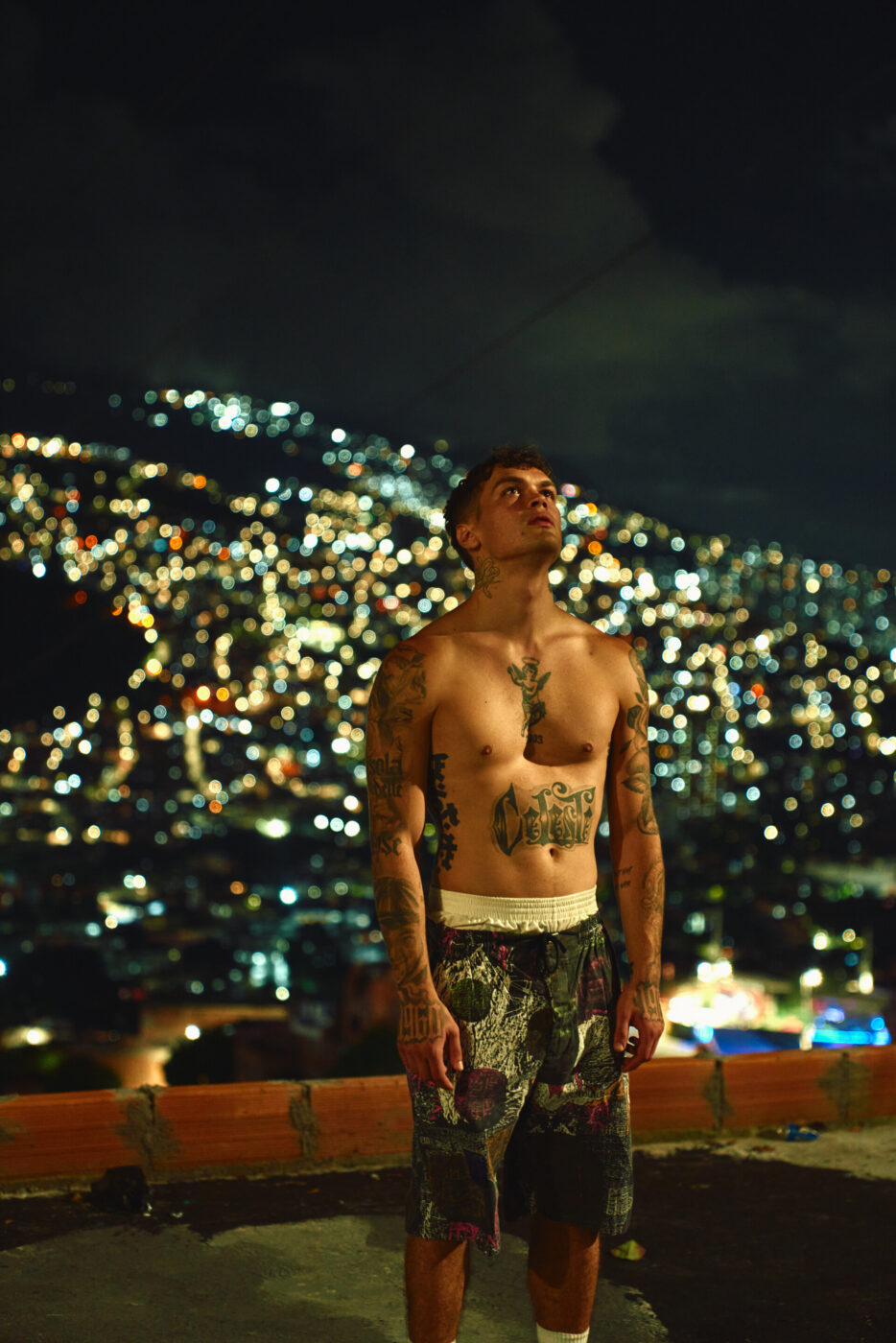 a man full of tattoo bare-chested, on a night roof