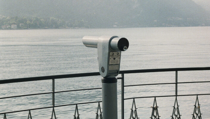 an image of a telescope by a railing at lake como