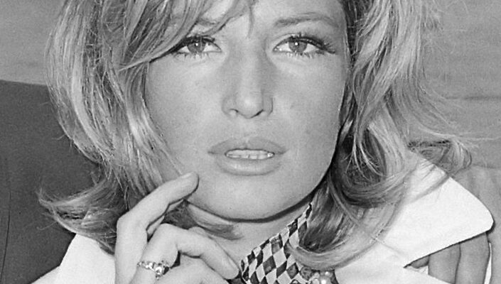 A black and white image of Monica Vitti in the movie Terence Stamp (1965) wearing a white blazer and holding her hand up towards her face