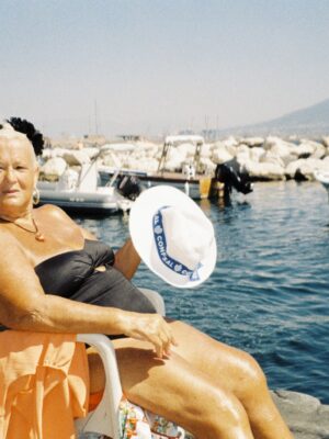 Blonde woman wearing black bathing suit sitting on plastic white chair by the sea