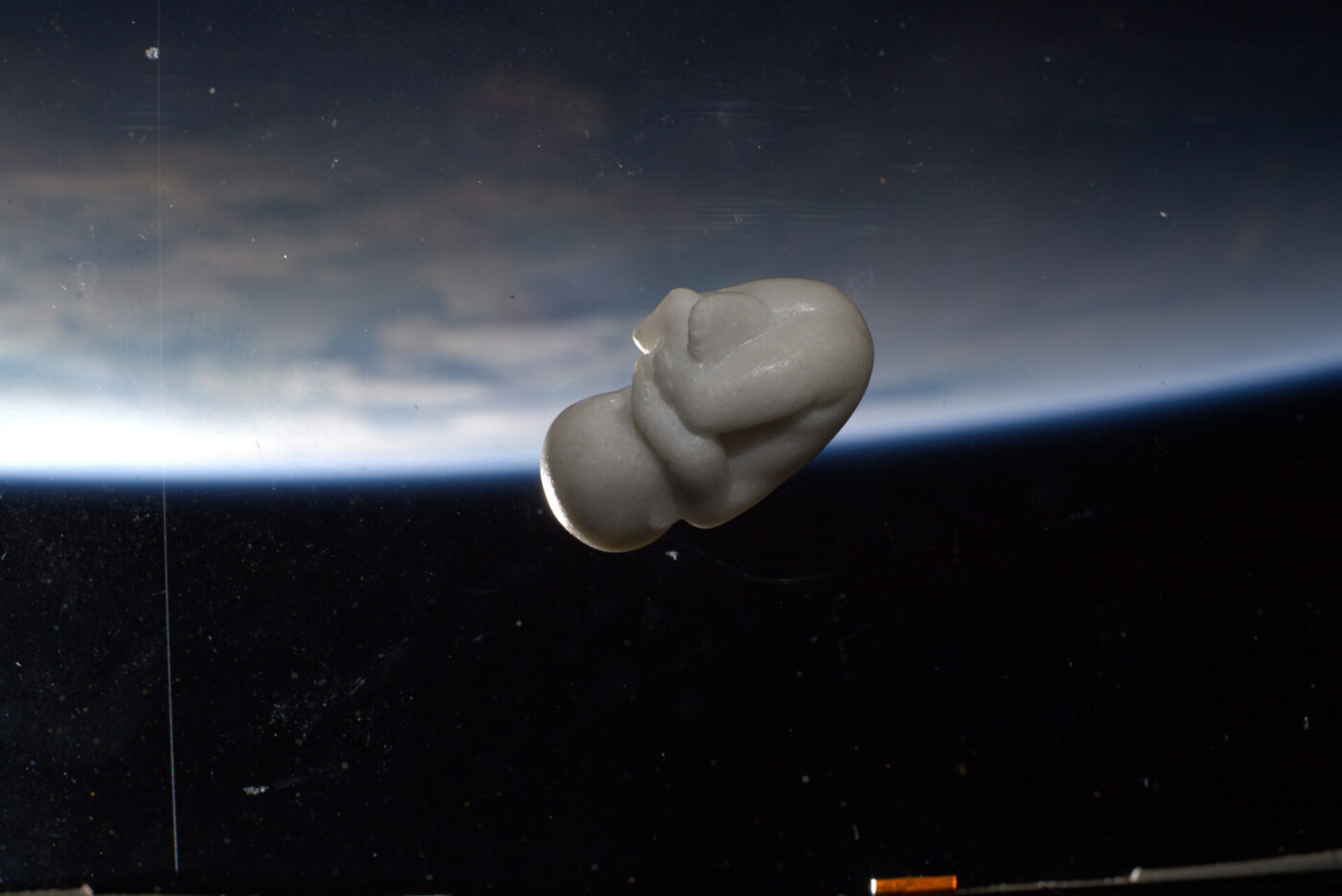 White detailed sculpture of a child fetus by Jago floating with a space picture of the earth
