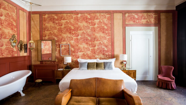 a room at Oltrarno Splendid with a clawfoot tub, large bed, tan loveseat couch against the foot of the bed, and light pink wallpaper