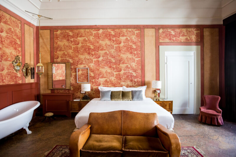 a room at Oltrarno Splendid with a clawfoot tub, large bed, tan loveseat couch against the foot of the bed, and light pink wallpaper