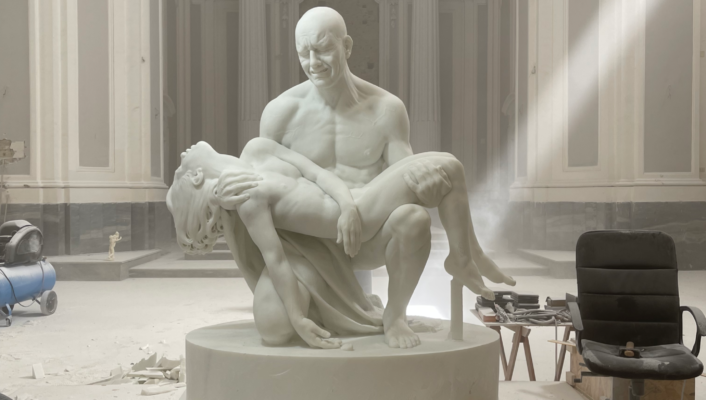 White sculpture of bald men down on his knees holding a woman's body like Michelangelo’s Pietà in a church studio with antique background in Napoli Campania in Italy