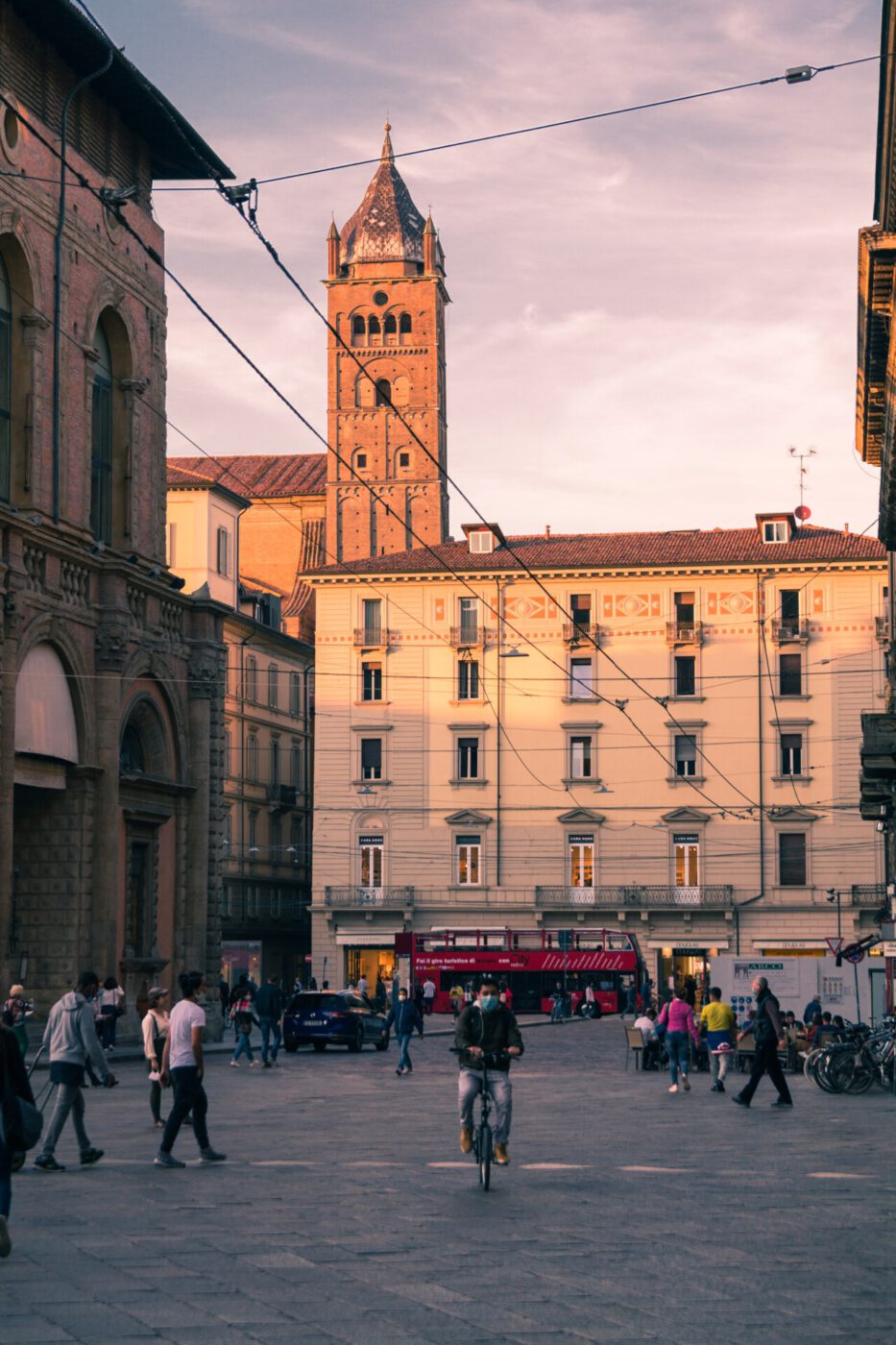 a man riding a bike through a piazza at dusk in Bologna, Italy