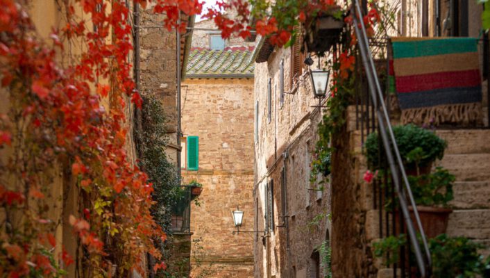 Antique narrow street with buildings on old bricks and stairs covered in plants and red leaves in autumn in Pienza Tuscany in Italy