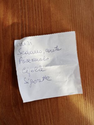 Handwritten grocery list in italian and blue ink over a post it paper and wooden table