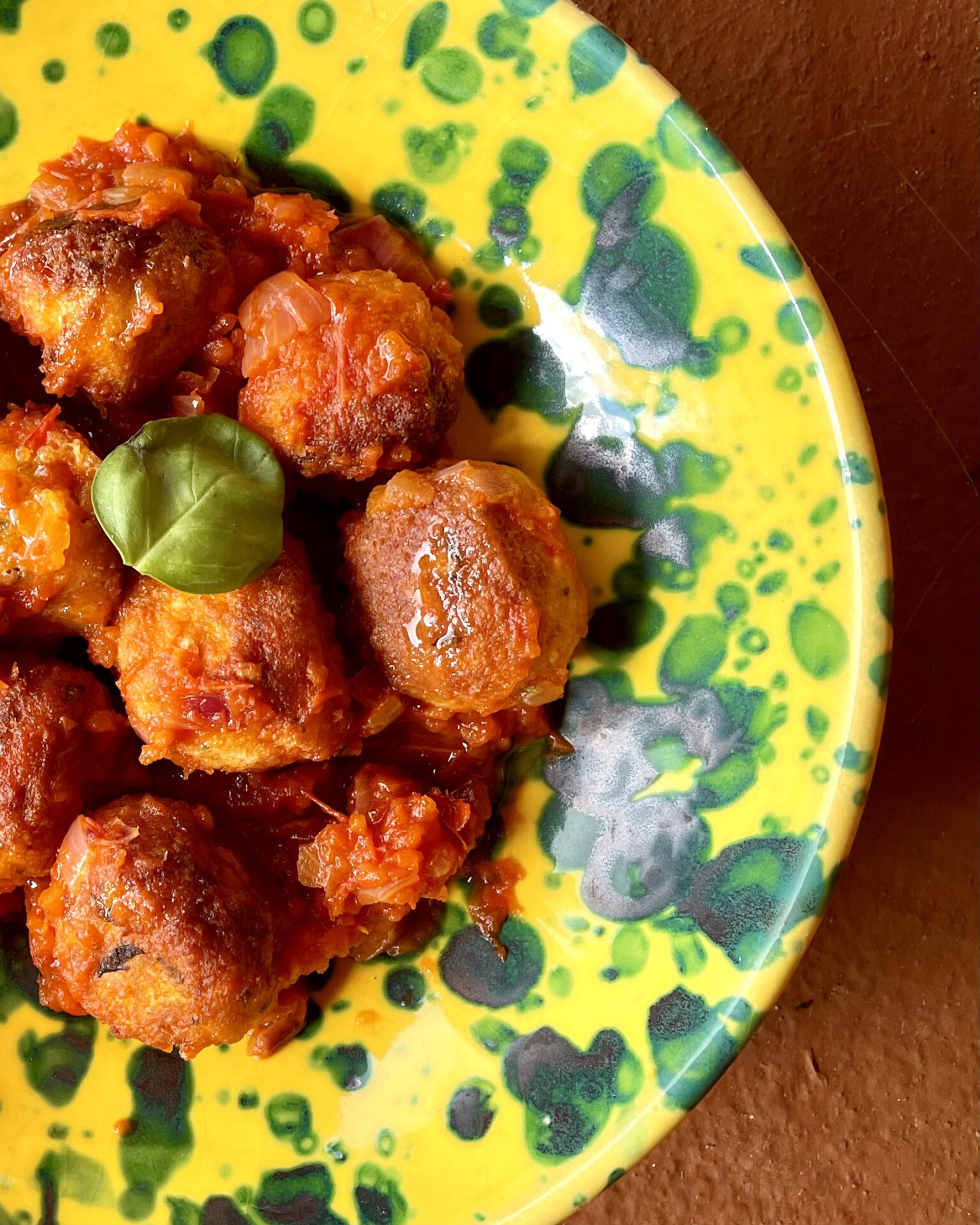 Italian homemade polpette meatballs over bright red tomato sauce and yellow ceramic plate in Italy