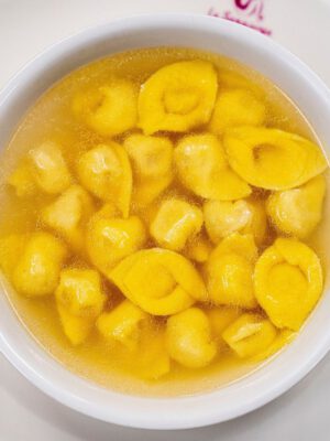 Yellow fresh tortellini filled pasta in golden clear broth in an italian restaurant in Emilia romagna