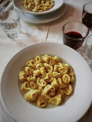 Handmade filled fresh tortellini pasta over yellow bright broth in plates next to wine and water cups in Emilia Romagna in Italy
