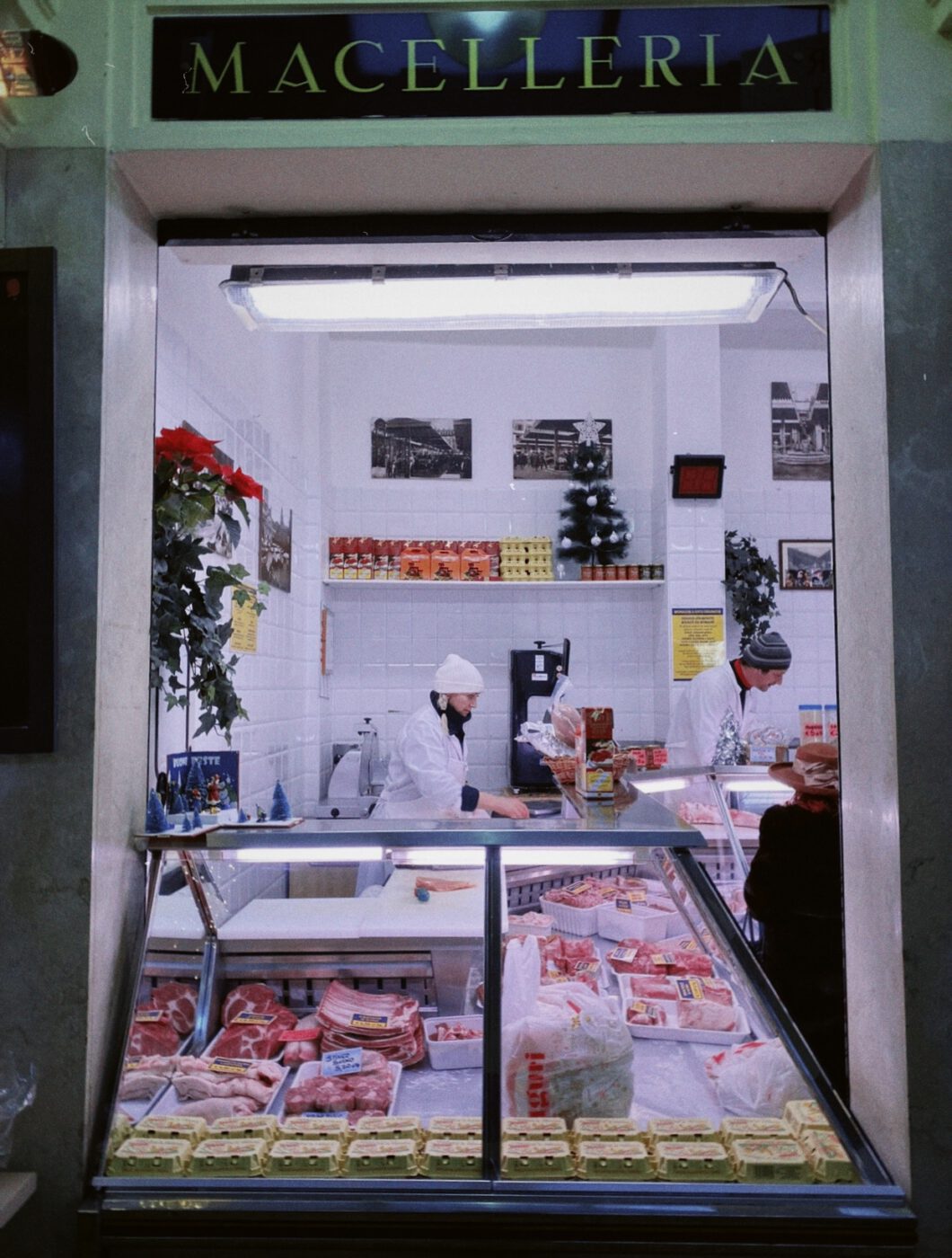 Typical butcher shop with glass counters filled up with meat and eggs white ceramic walls and people buying in Emilia Romagna in Italy