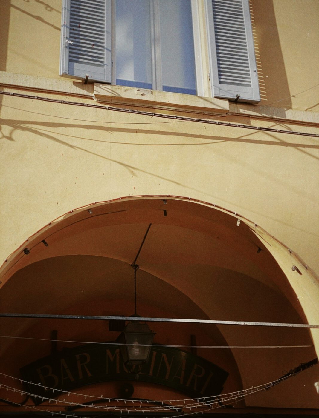 Yellow arched roof and wall with wooden window and cables crossing in Emilia Romagna Italy