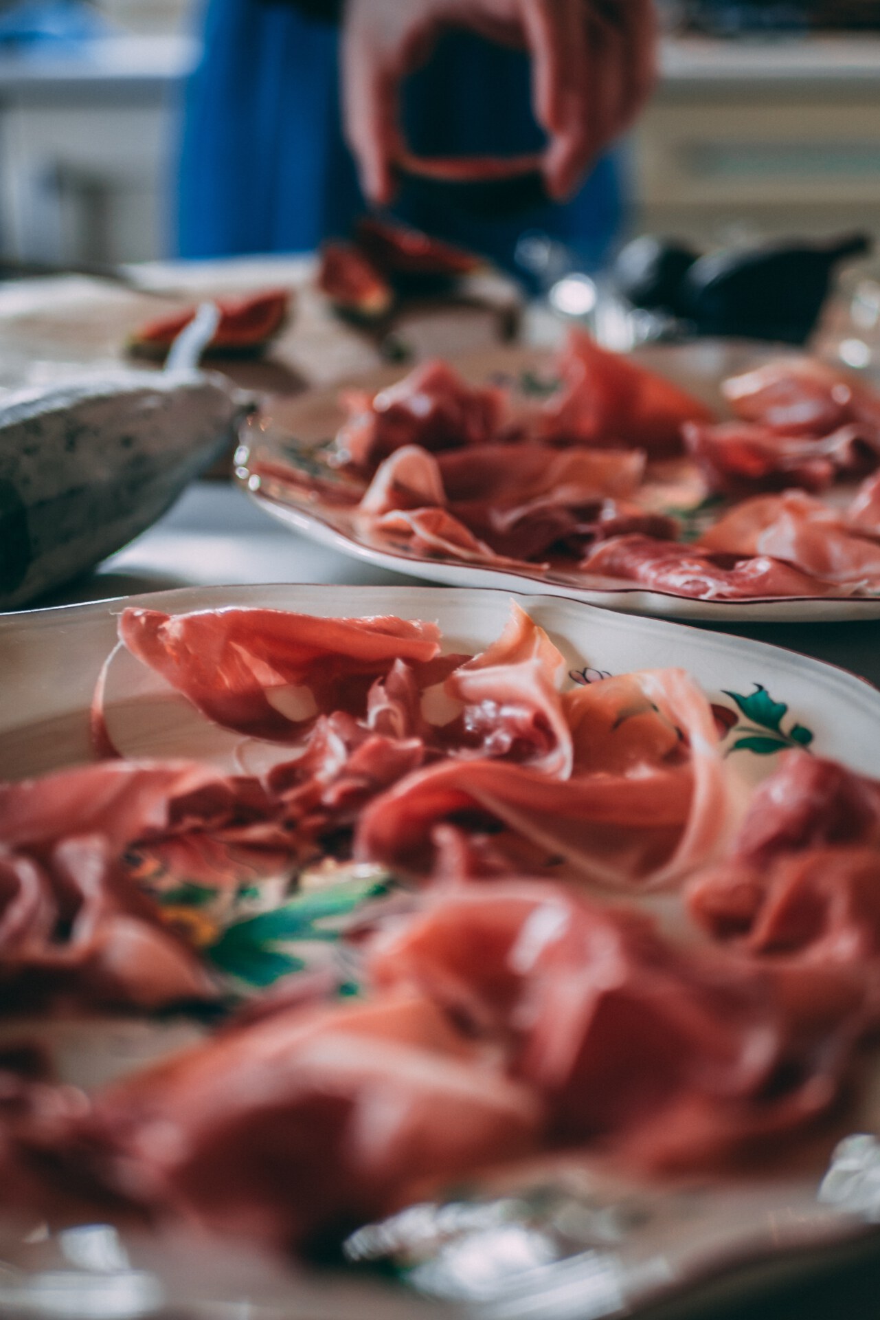 Thin slices of raw prosciutto di parma over colorful ceramic plates and figs fruit in a typical italian kitchen