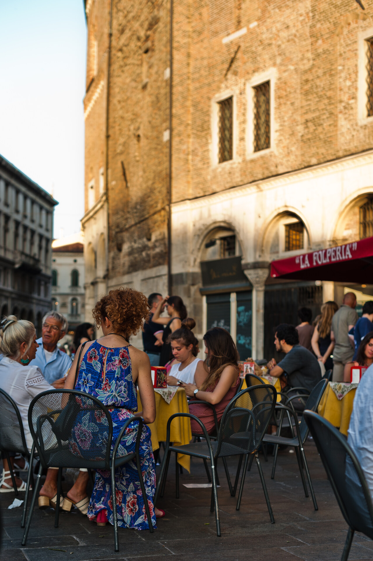 People seated at metallic tables and chairs with a old antique building in cricks background at la folperia kiosk restaurant in Padua Veneto in Italy