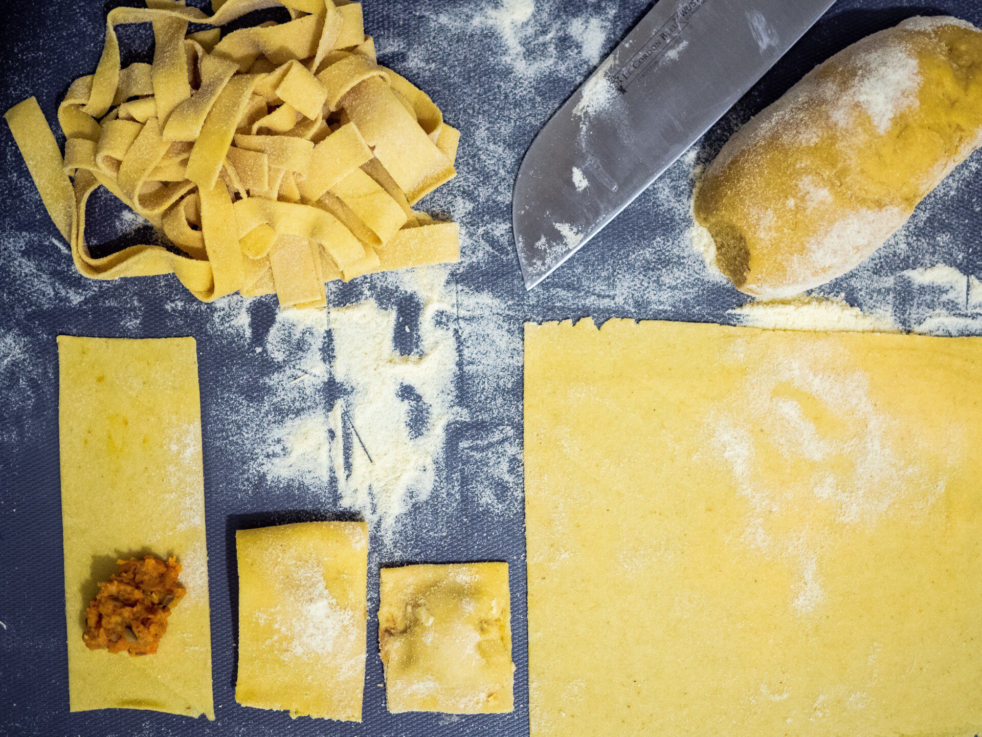 Fresh pasta dough cut in fettuccine and rectangles being filled with meat filling for ravioli di magro in Italy