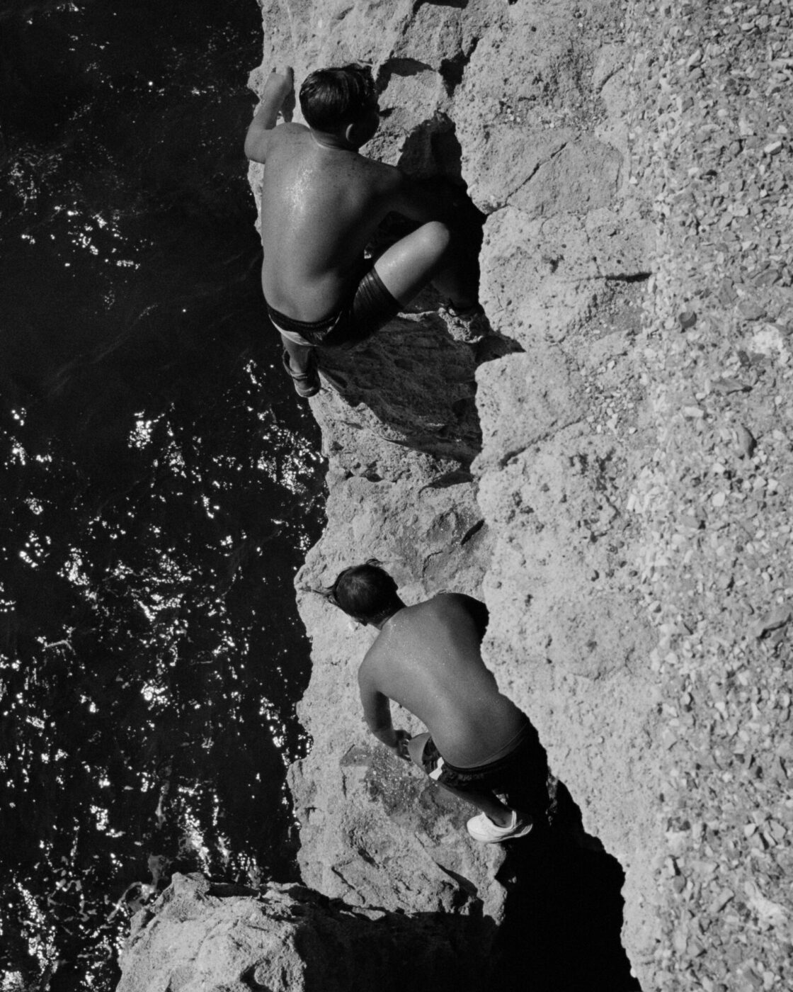 Two men over rocks at the sea in Black & White at Napoli Campania in Italy, photographed by Brett Lloyd