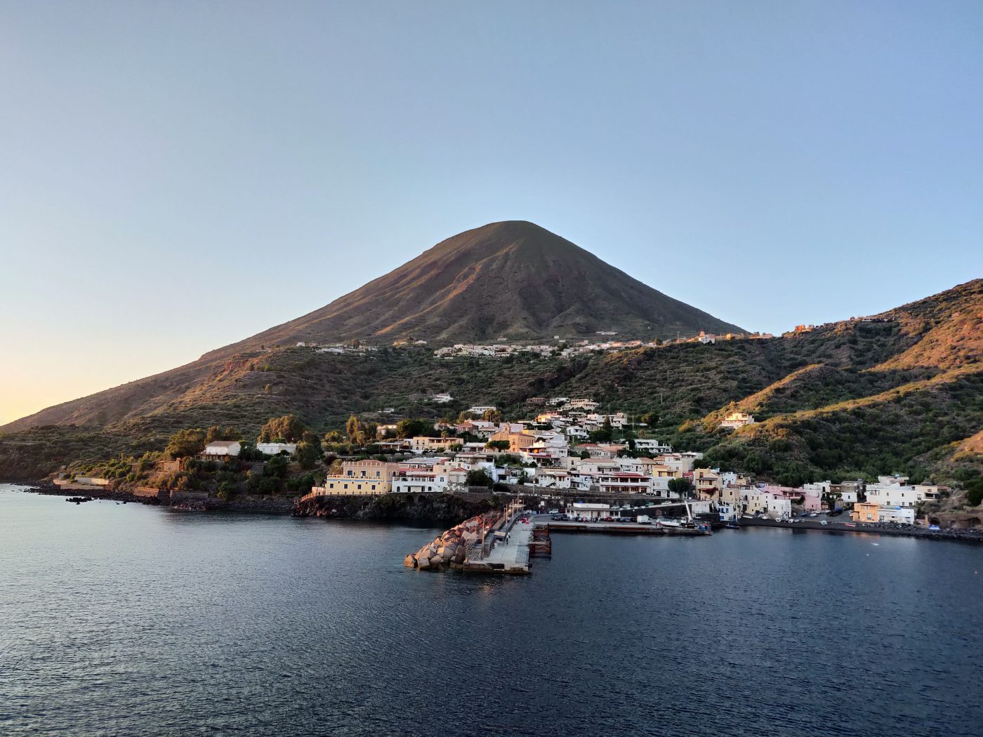 a small island off the coast of Sicily with a volcano and long dock leading to a smalFILICUDI On the smallest of the Aeolian Islands, don’t expect glitz nightclubs, sandy beaches, or 5-star hotels. But what it lacks in comfort, it makes up for in authenticity: which is, nowadays, such a rare, covetable luxury. WHERE TO SLEEP ON FILICUDI Casa G – This house on the exceptional island has four double bedrooms and bathrooms in an equal number with a 360º terrace overlooking only the sea. WHERE TO EAT ON FILICUDI La Sirena – In the bay of Percorini a Mare, La Sirena is a simple, local spot with an excellent location right on the sea. Don’t miss trying the Sicilian staple caponata or their spaghetti with almonds. l, light up town