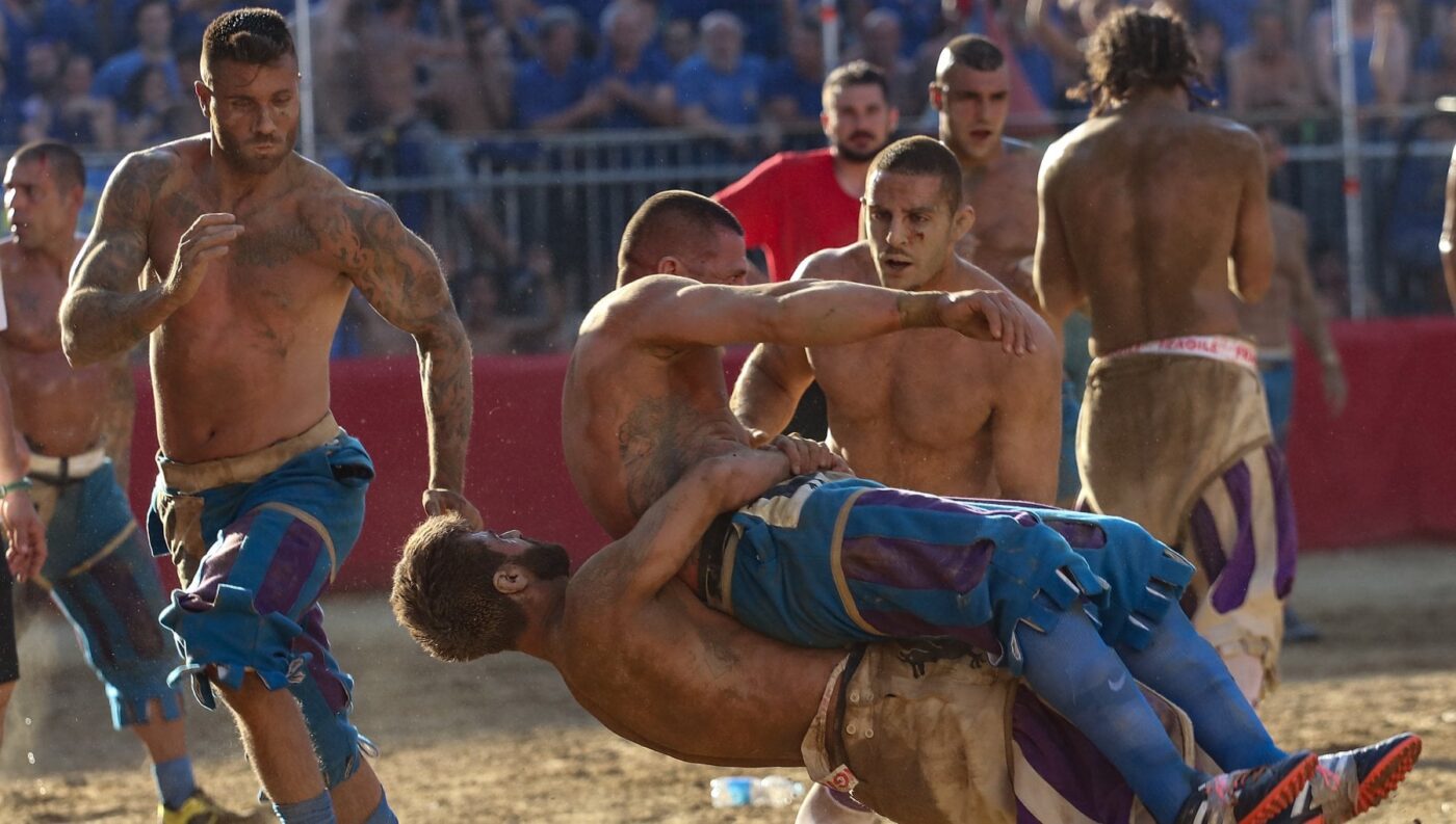 shirtless and covered-in-dirt men getting tackled while playing in the Calcio Storico