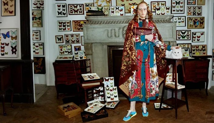 a model wearing a colorful Gucci piece in a room full of taxidermy butterflies