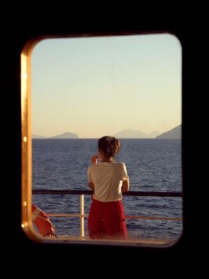 photo by Michele Iacobini through the window of a boat of a woman looking out over the water and islands as the sun sets