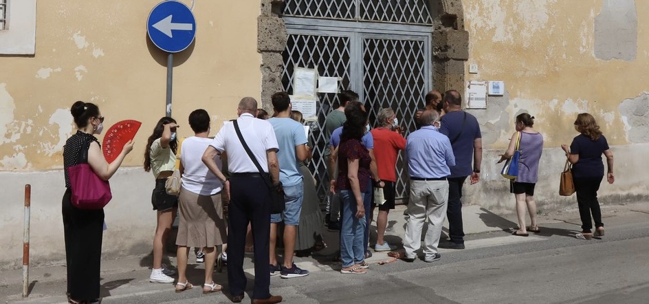 a large group of people crowding outside of an Italian bureaucratic building
