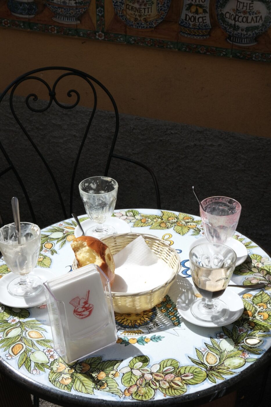 a small table with typical Sicilian patterning in the sun with empty gelato and granita cups and one remaining brioche