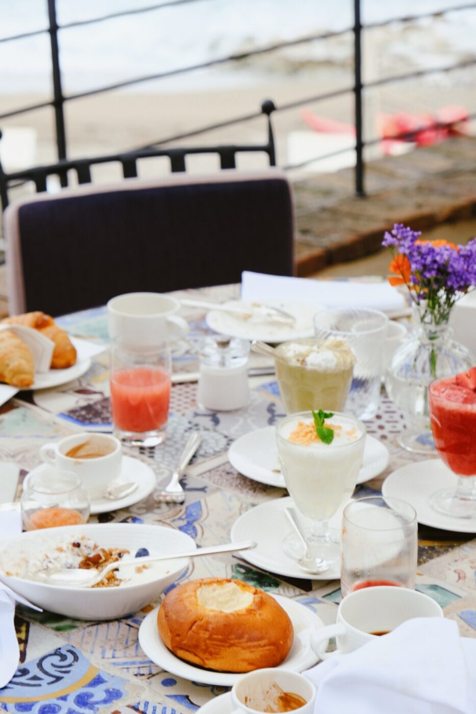 a breakfast table on a terrace with a bright tablecloth, empty glasses of grapefruit juice and half-eaten yogurt and pastries