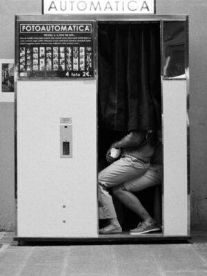 Firenze '20 vanità di coppia; a black and white photo by Francesco Serpico of an photobooth with a couple sitting on each others lap