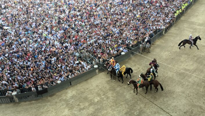 horses running along the track and crowd of people in the Palio di Siena