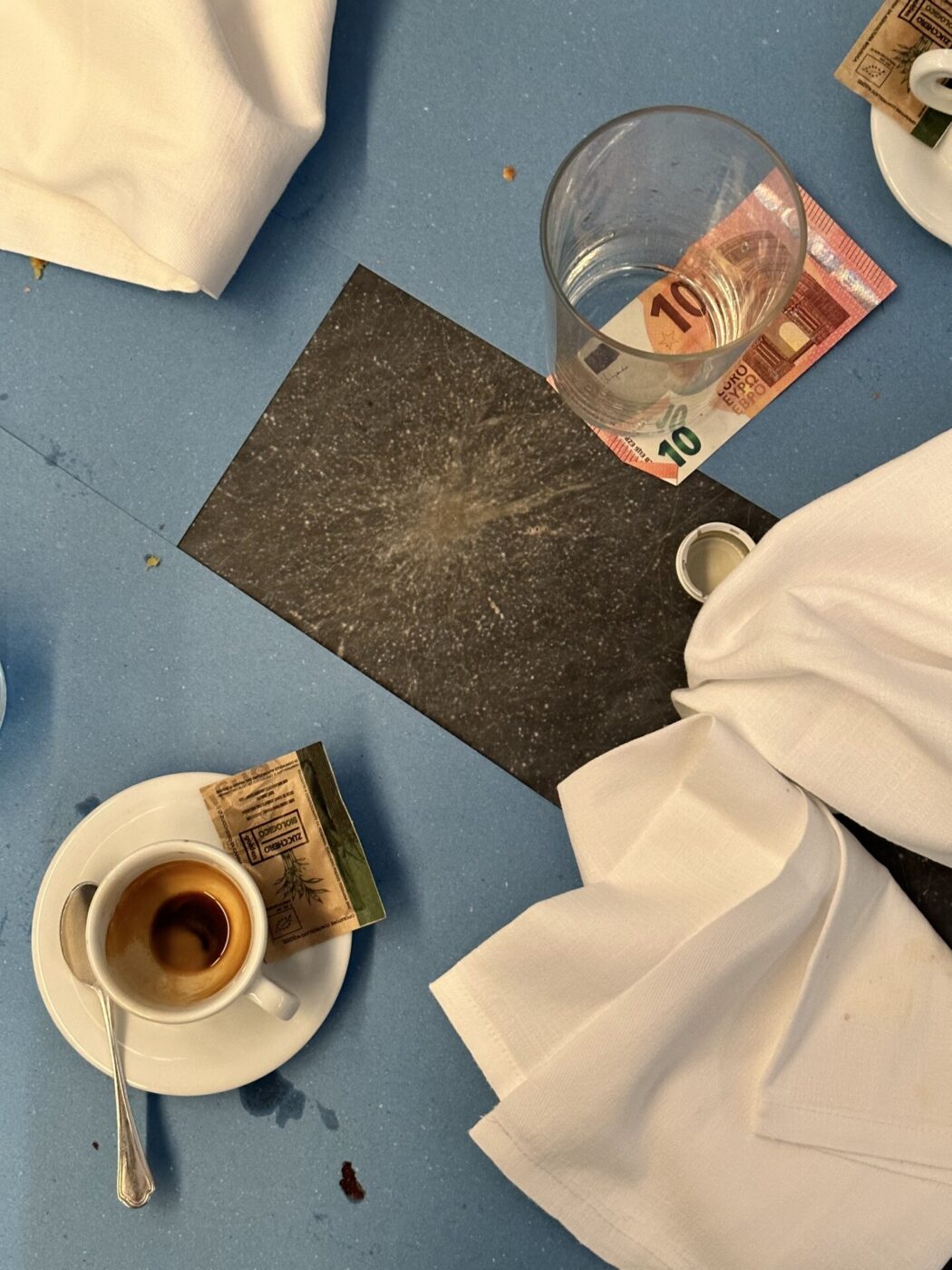 Picture of a table after a meal showing an empty espresso cup and a 10 euro stuck under a water glass