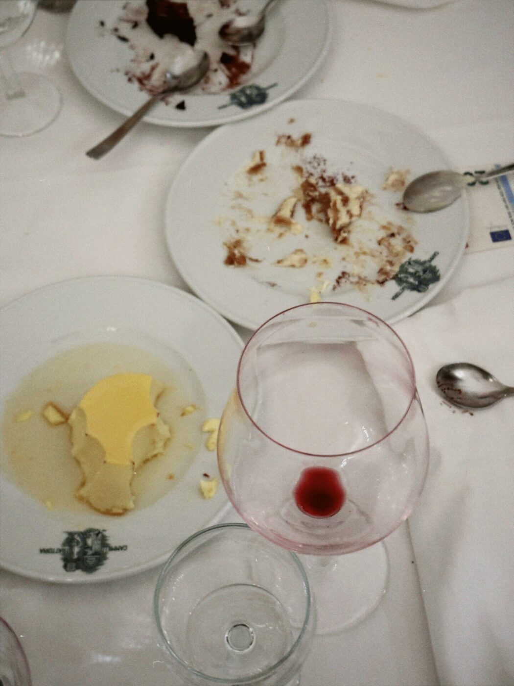 three nearly finished plates of dessert and an empty glass of wine left at a table after a meal